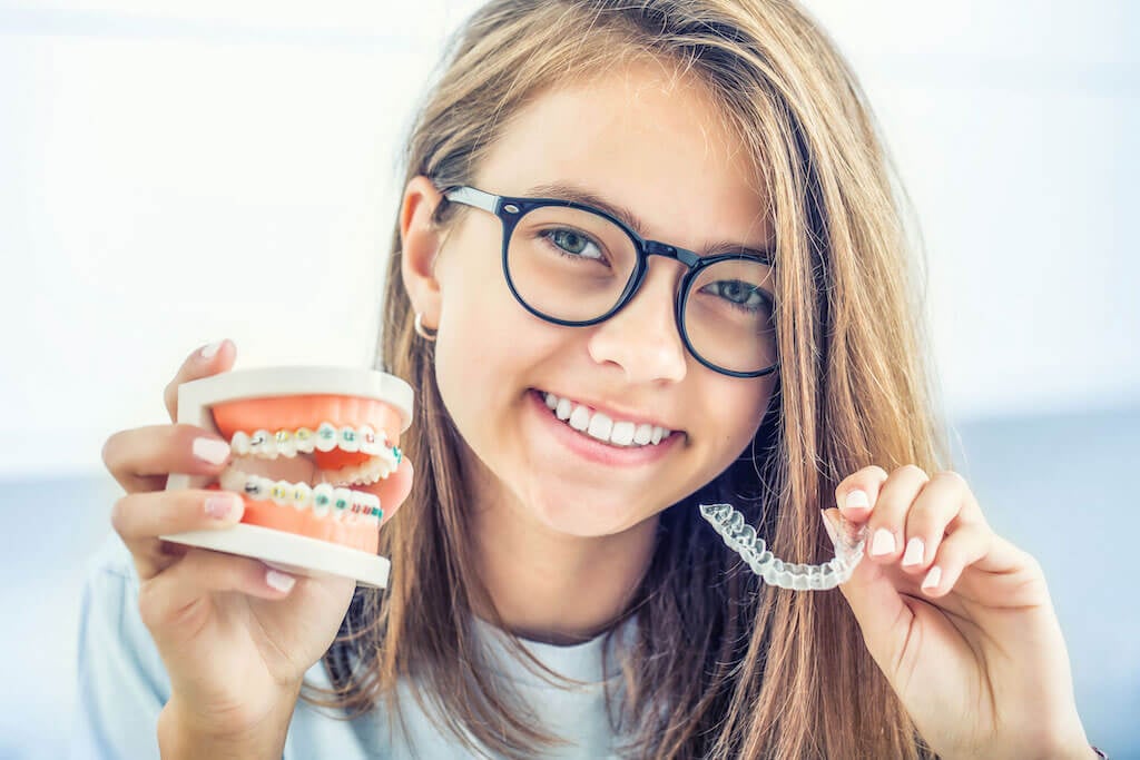 girl holding invisalign next to traditional braces